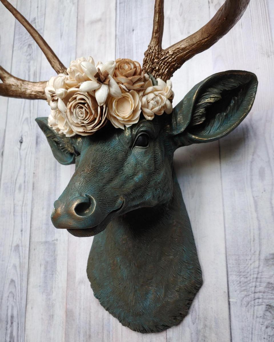 Faux taxidermy deer head painted verdigris with antique gold antlers. A floral crown made of cream sola flowers rests atop the deers head