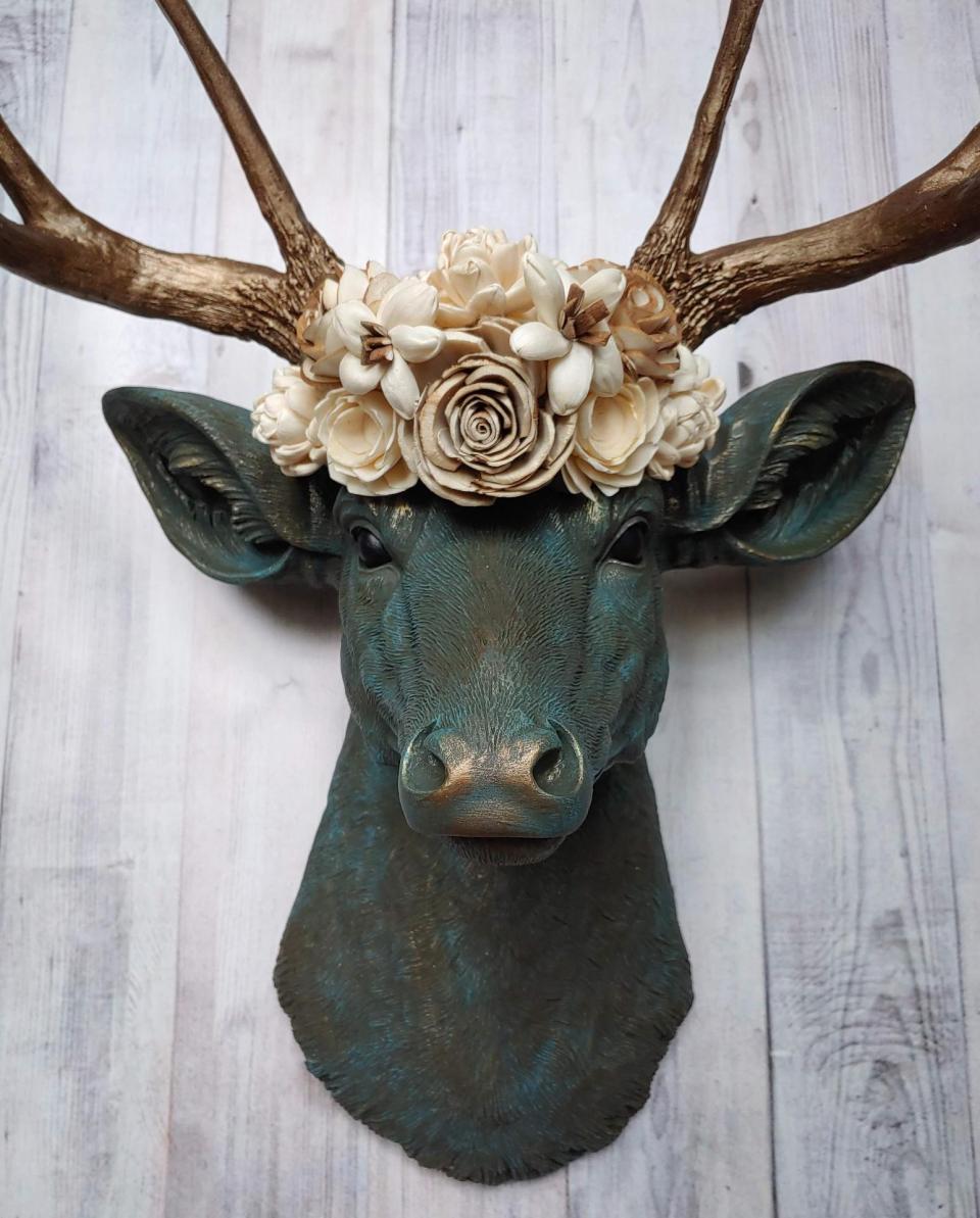 Faux taxidermy deer head painted verdigris with antique gold antlers. A floral crown made of cream sola flowers rests atop the deers head