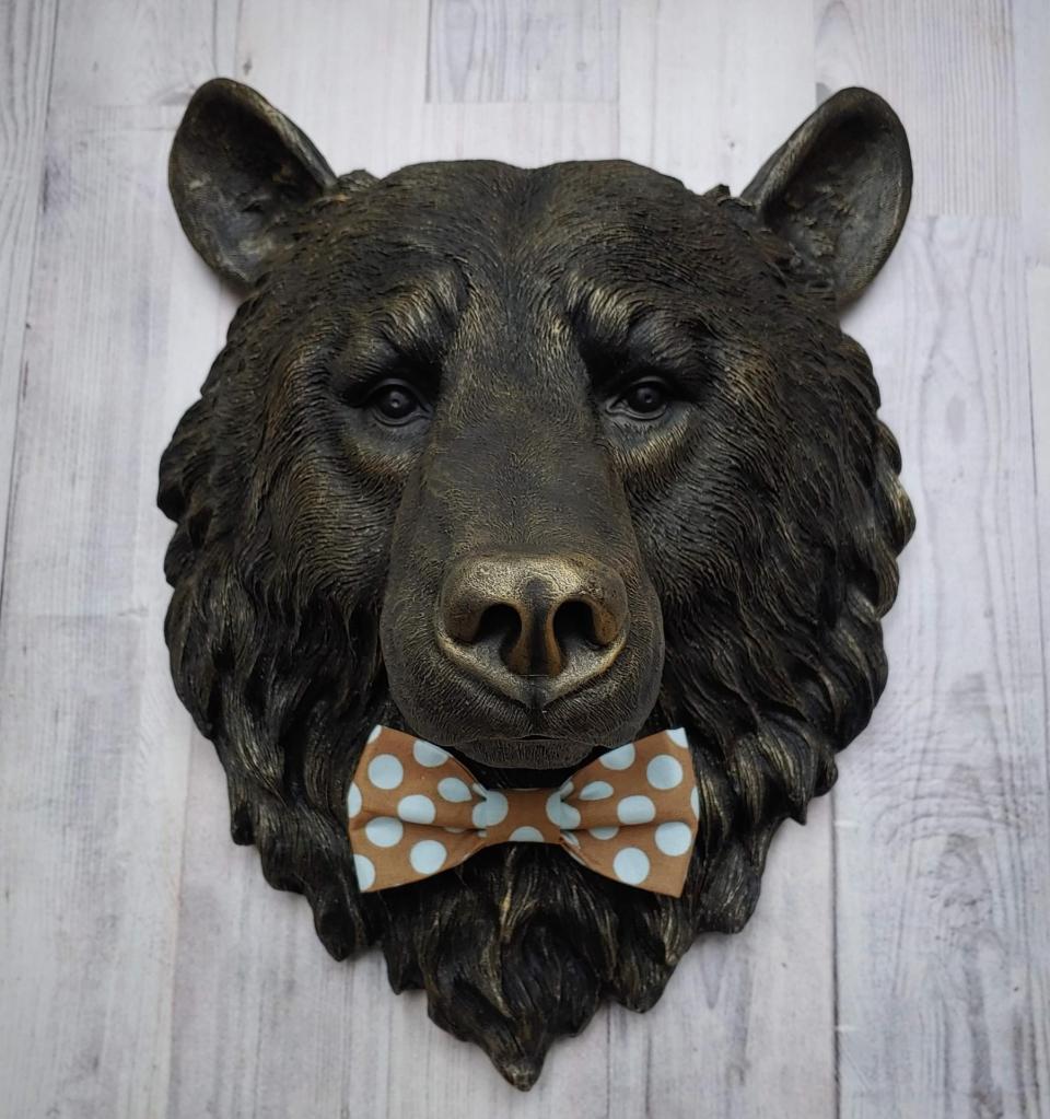 Faux taxidermy bear head wall mount, painted black with gold accenting. A brown and blue polka dot fabric bow tie accents the bears neck