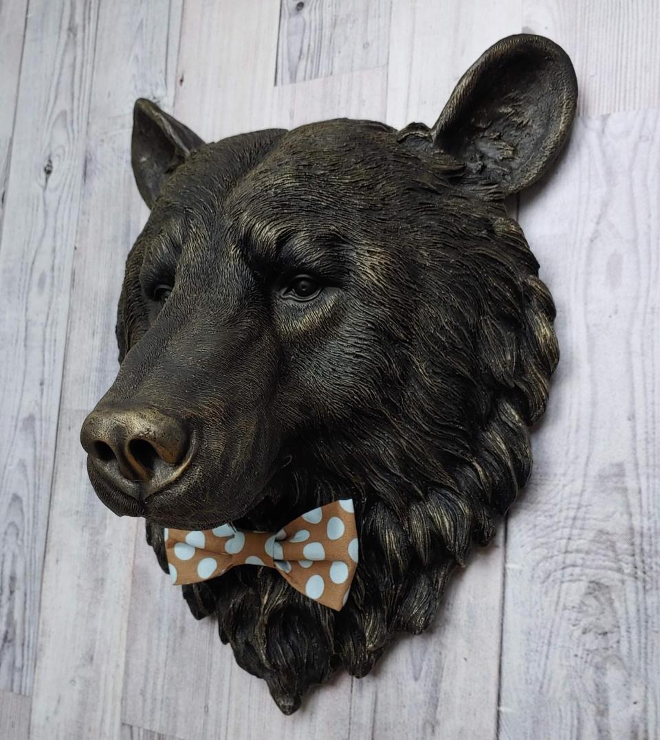 Faux taxidermy bear head wall mount, painted black with gold accenting. A brown and blue polka dot fabric bow tie accents the bears neck