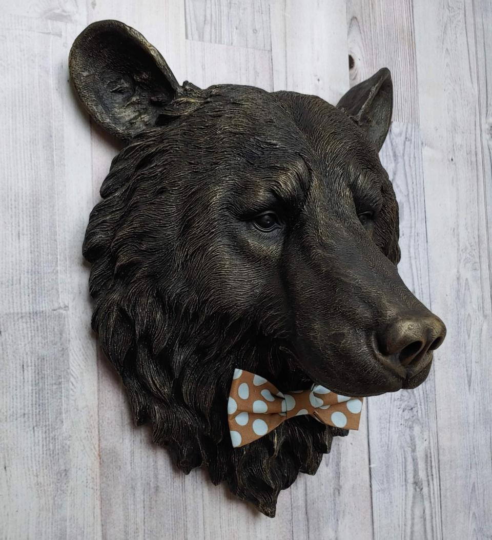 Faux taxidermy bear head wall mount, painted black with gold accenting. A brown and blue polka dot fabric bow tie accents the bears neck