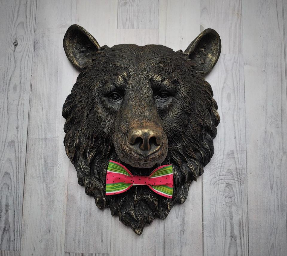 Faux taxidermy bear head wall mount, painted black with gold accenting. A watermelon print fabric bow tie accents the bears neck.