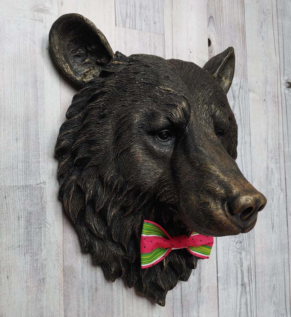 Faux taxidermy bear head wall mount, painted black with gold accenting. A watermelon print fabric bow tie accents the bears neck.