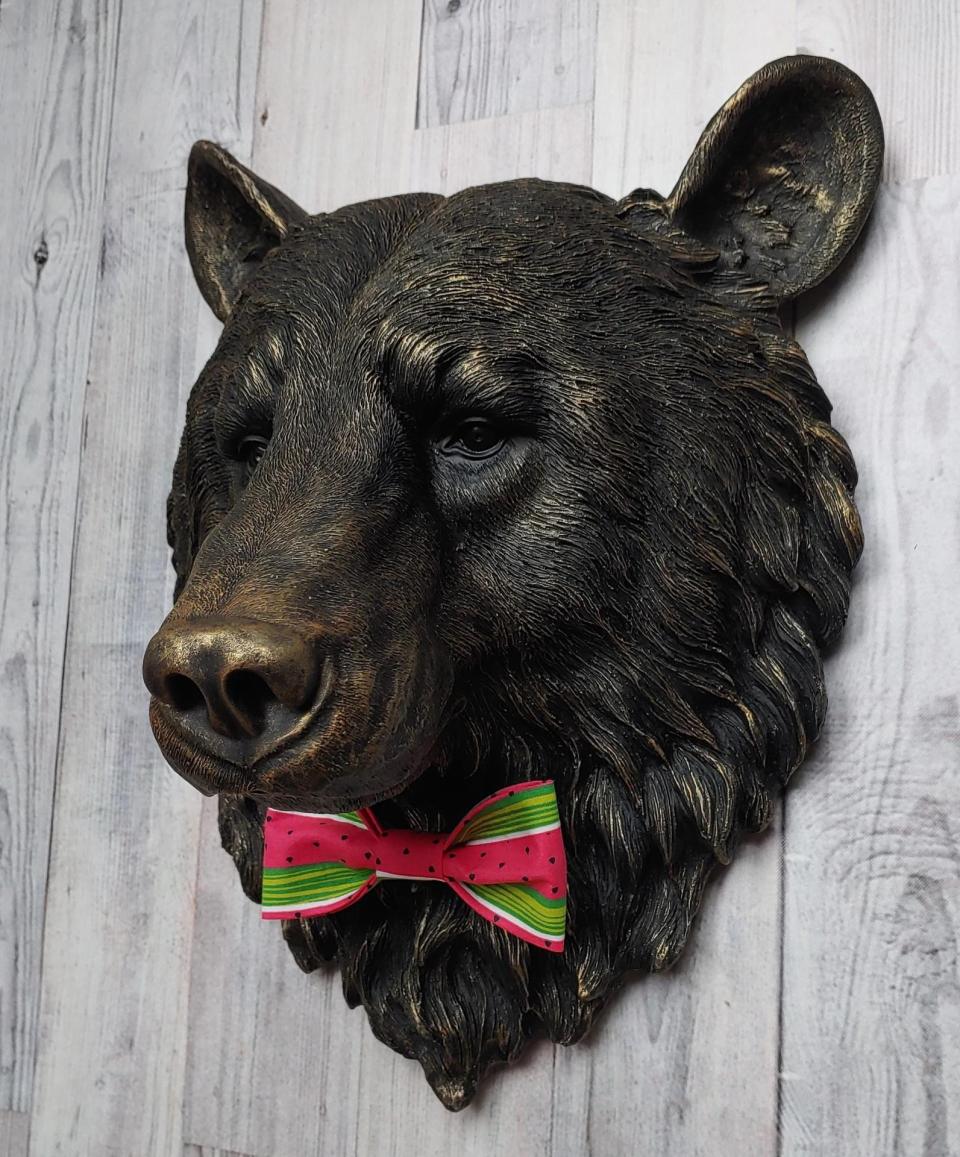 Faux taxidermy bear head wall mount, painted black with gold accenting. A watermelon print fabric bow tie accents the bears neck.