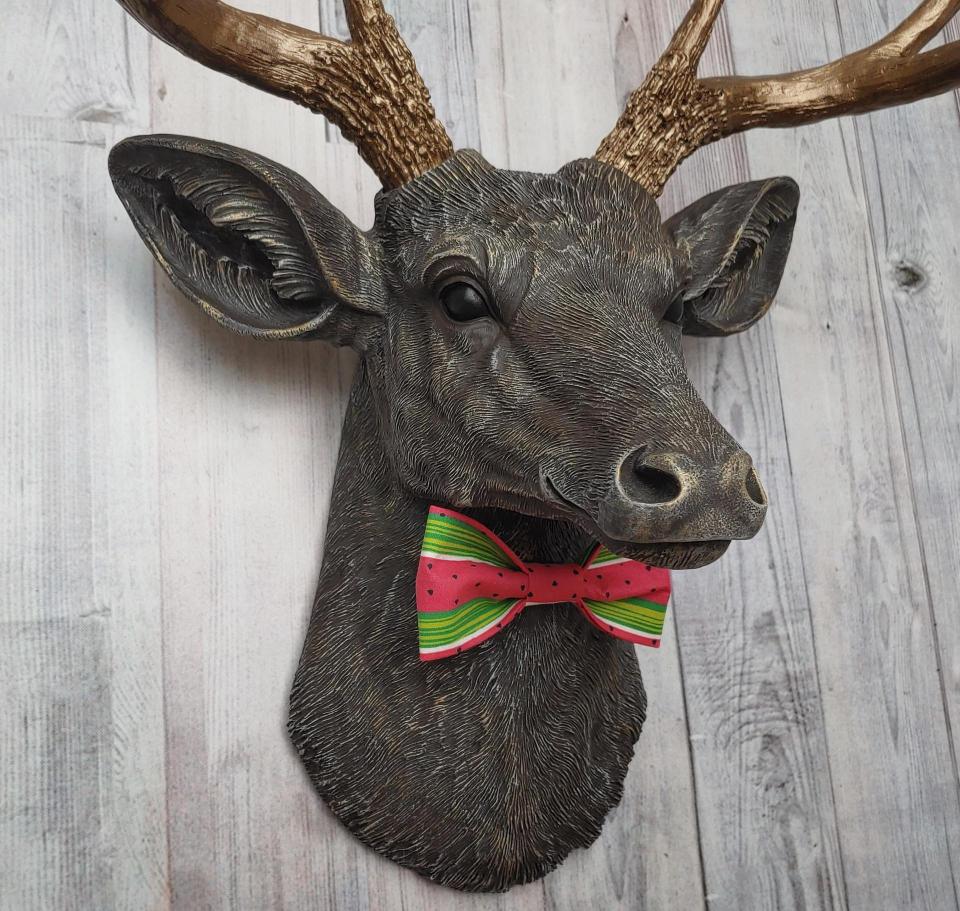 Faux taxidermy deer head painted chestnut brown and accented with antique white and antique gold. The antlers have been painted antique gold and the eyes have been painted black.Watermelon print fabric bow tie accents the deers neck.