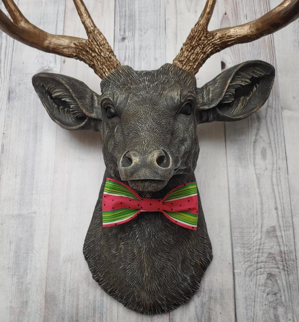 Faux taxidermy deer head painted chestnut brown and accented with antique white and antique gold. The antlers have been painted antique gold and the eyes have been painted black.Watermelon print fabric bow tie accents the deers neck.