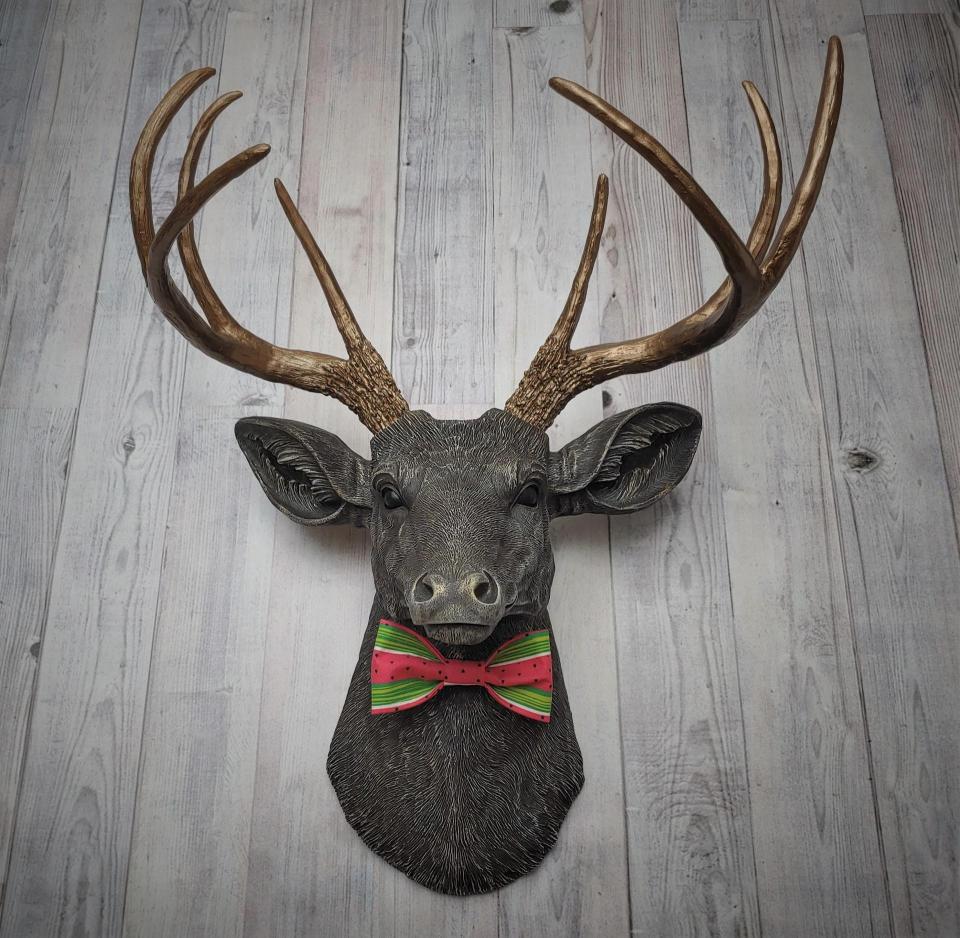 Faux taxidermy deer head painted chestnut brown and accented with antique white and antique gold. The antlers have been painted antique gold and the eyes have been painted black.Watermelon print fabric bow tie accents the deers neck.