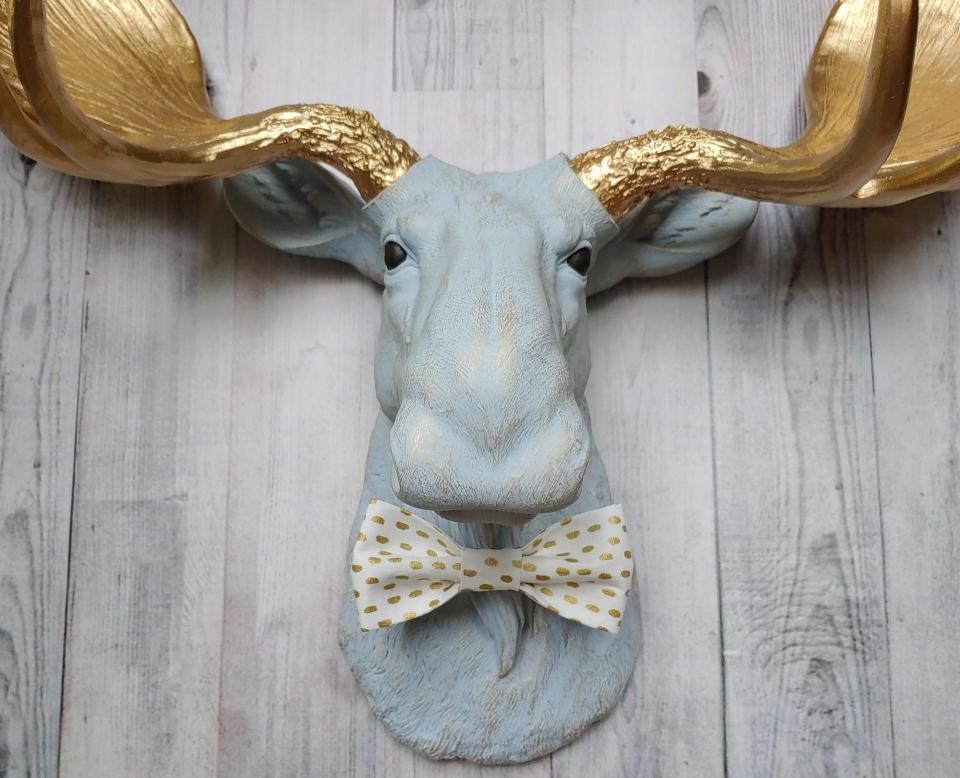Faux taxidermy moose head painted winter blue with gold antlers with a white and gold polka dot bow tie.