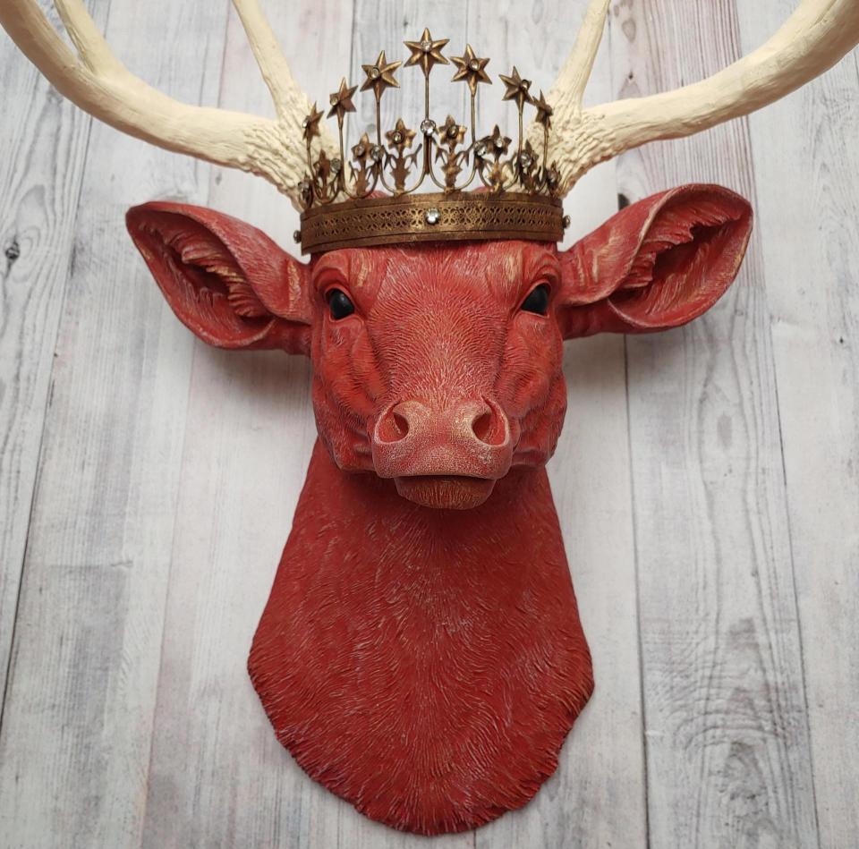 Faux taxidermy deer head, painted red with antique white antlers with a bronze Santos crown atop its head.