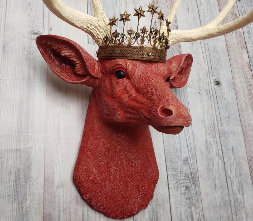 Faux taxidermy deer head, painted red with antique white antlers with a bronze Santos crown atop its head.
