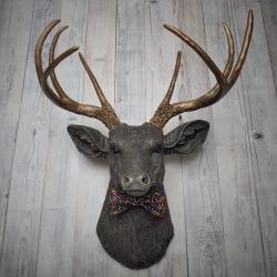 Faux taxidermy dee head painted chestnut brown and accented with antique white and antique gold. The antlers have been painted antique gold and the eyes have been painted black. A fabric bow tie that has a black background with multi colored sprinkles accents the deers neck.